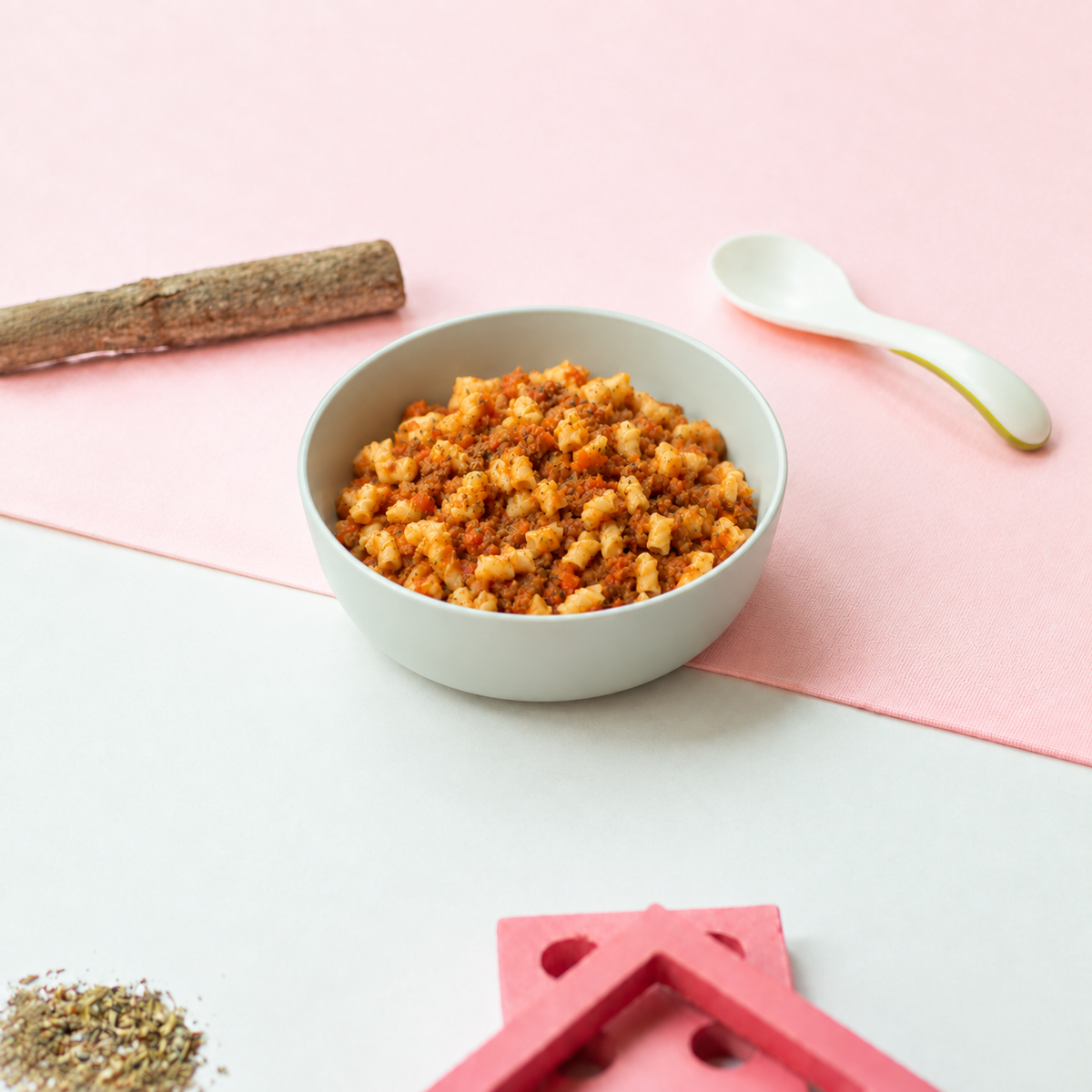 Small-cut Bolognese pasta with minced beef and tomato sauce in a light-grey child-sized bowl