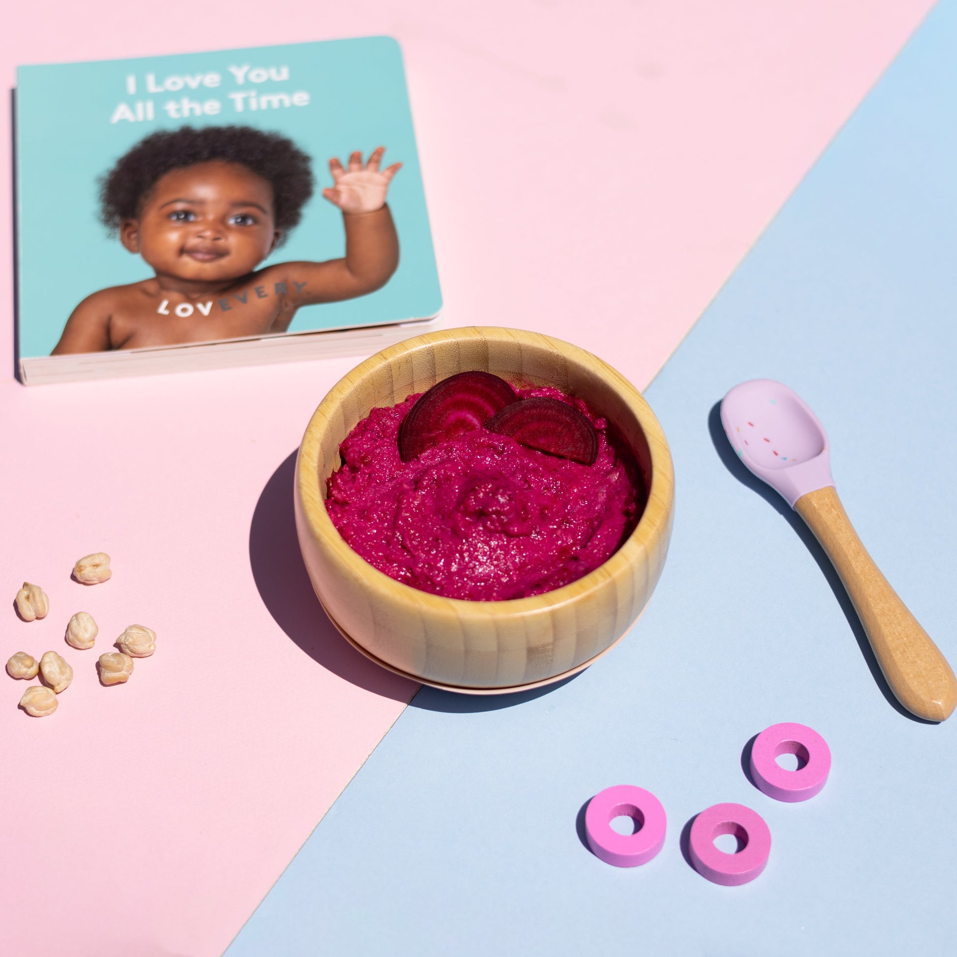 Pink baby food in a wooden bowl with a photo of a baby and a spoon on a pink and blue background