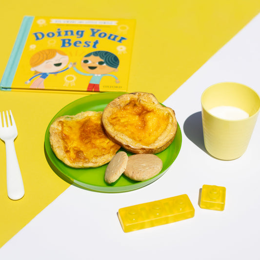 Children's book titled 'Doing Your Best' with a plate of food, cup, and toys on a yellow and white background.