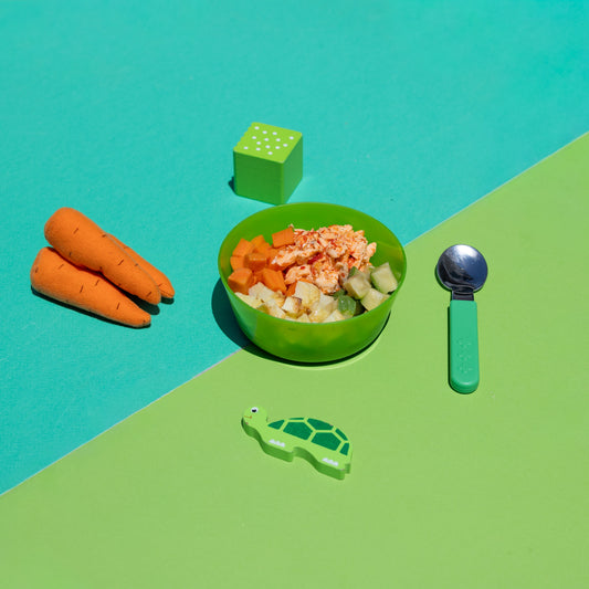 Green bowl with food, carrots, and a spoon on a green and blue background